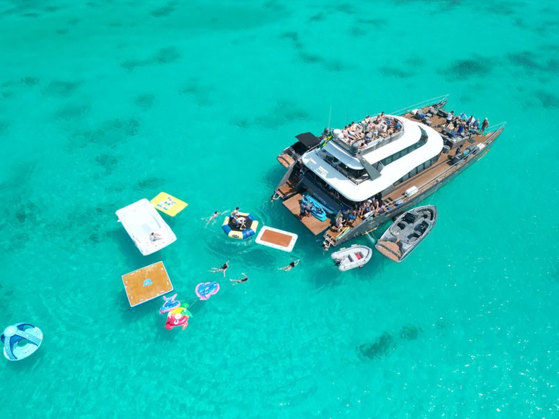 Aerial view of the 80ft Atlantis II catamaran in the Bahamas showing her twin hulls and a floating island alongside