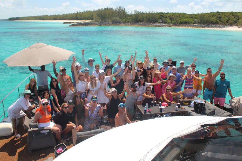 A large charter group gathered on the beach with the 80ft Atlantis II catamaran moored behind