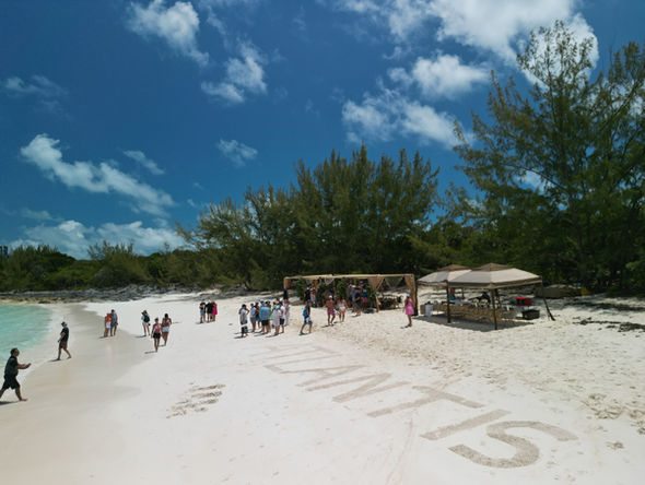 Guests on a Bahamian beach beside the yacht name written in the sand