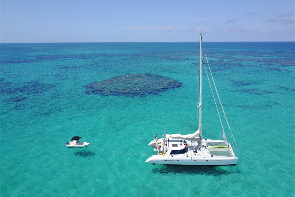 Charter catamaran anchored over a reef patch in clear Bahamian water