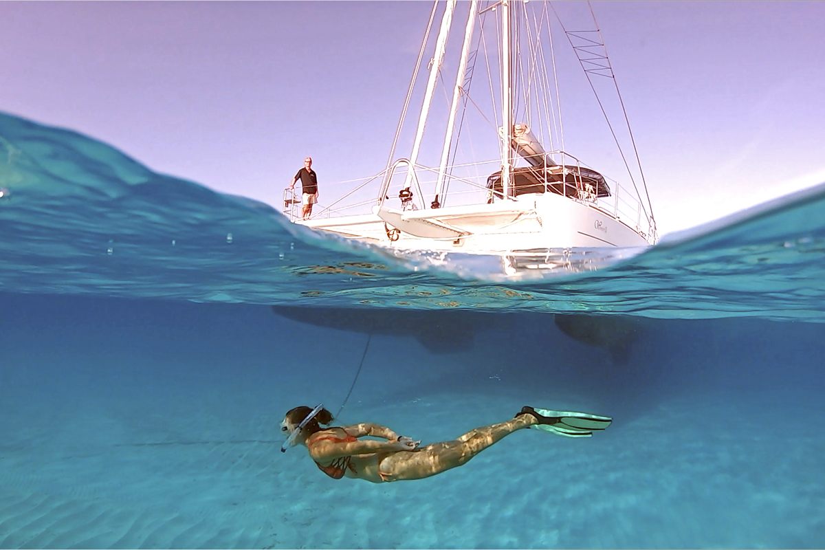 Snorkeller in clear water beside a sailing catamaran in the Bahamas